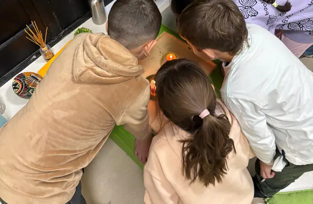 Chicos de espaldas, reunidos alrededor de una mesa durante una actividad del grupo de niños.