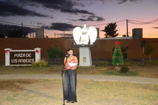La Plaza de Los Ángeles al atardecer, con la escultura del ángel y una mujer hablando al micrófono.
